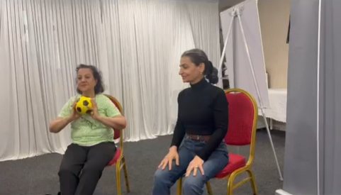 Two people taking part in a seated movement session with a soft ball.