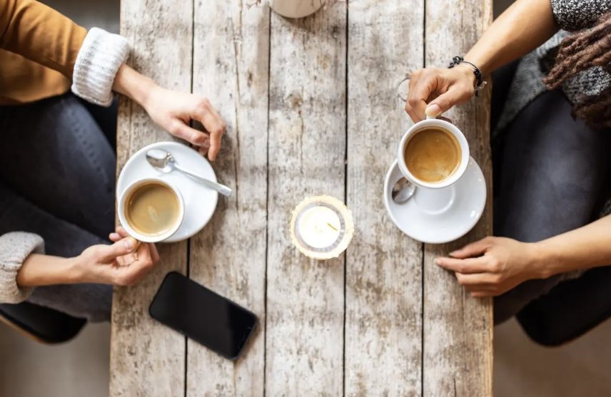 Two people sitting across a wooden table with cups of coffee.
